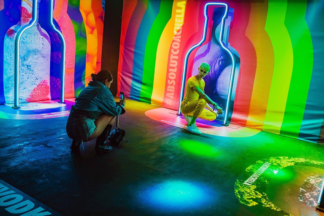 Person poses in front of Absolut rainbow light and banner. This was one of many colorful photo moments. 