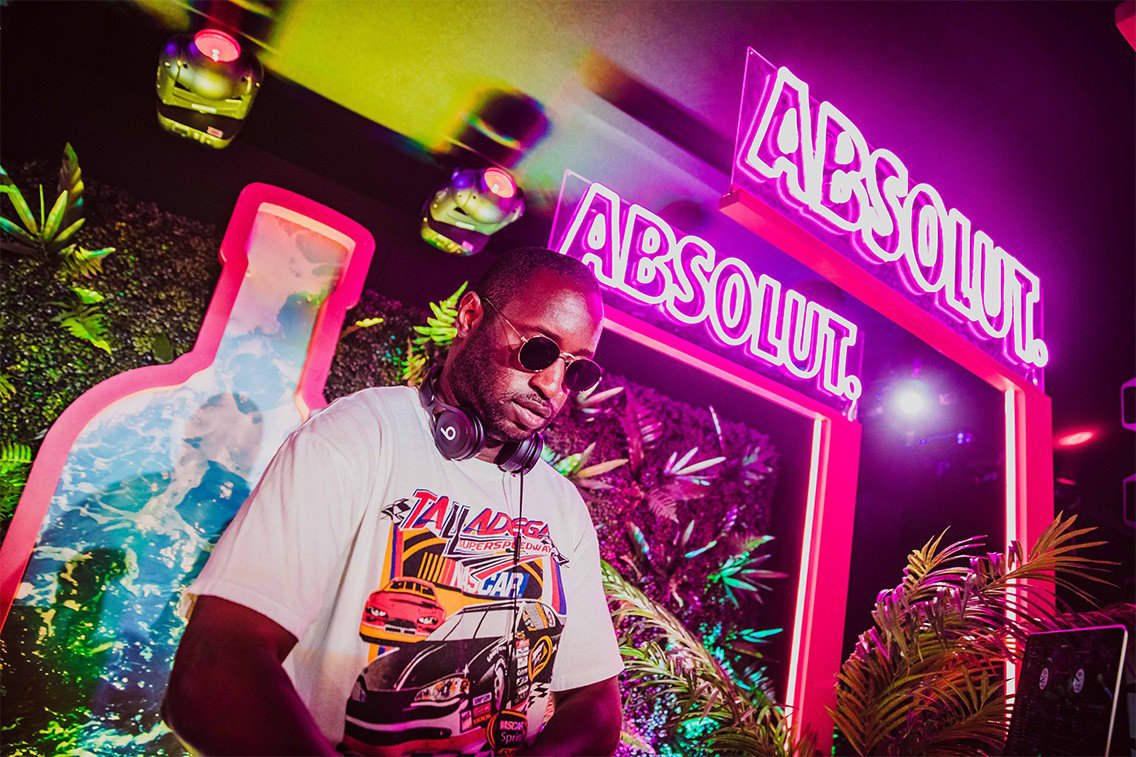DJ spins records in front of neon Absolut signage. The festival activation spread a message of acceptance for all. 