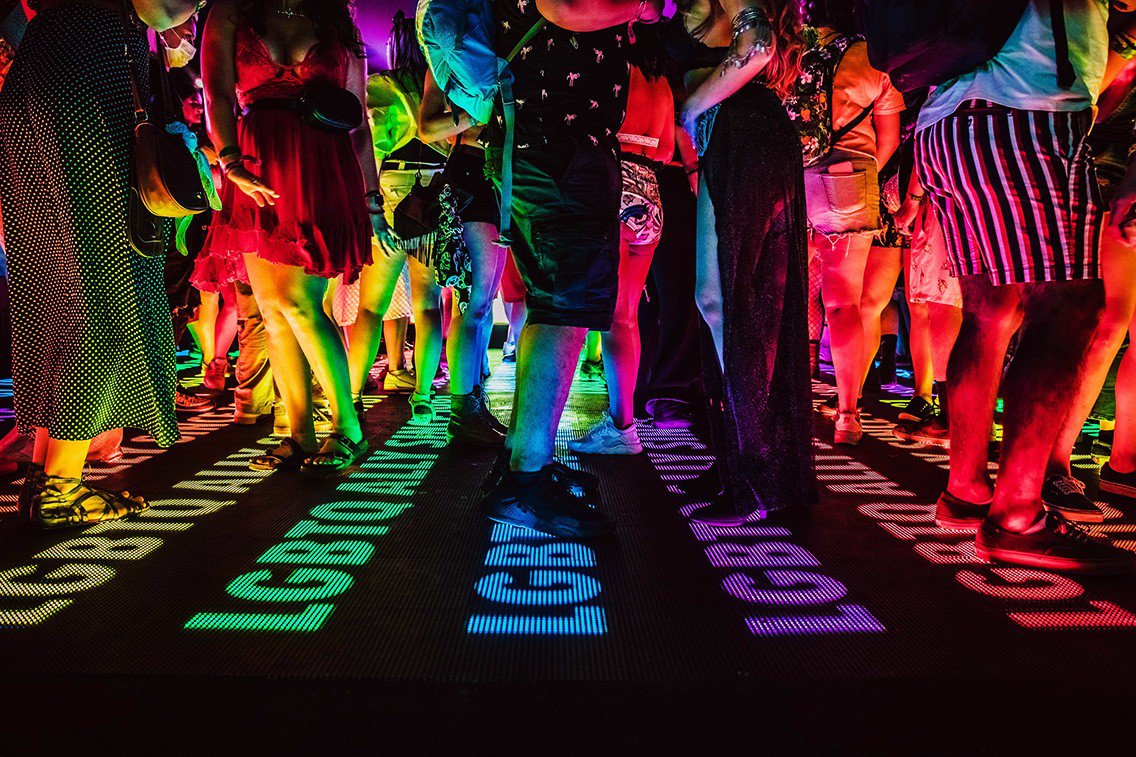 Event goers stand over a rainbow lit dance floor with LGBTQ Ally written in LEDs. The activation acted as an oasis in the desert.