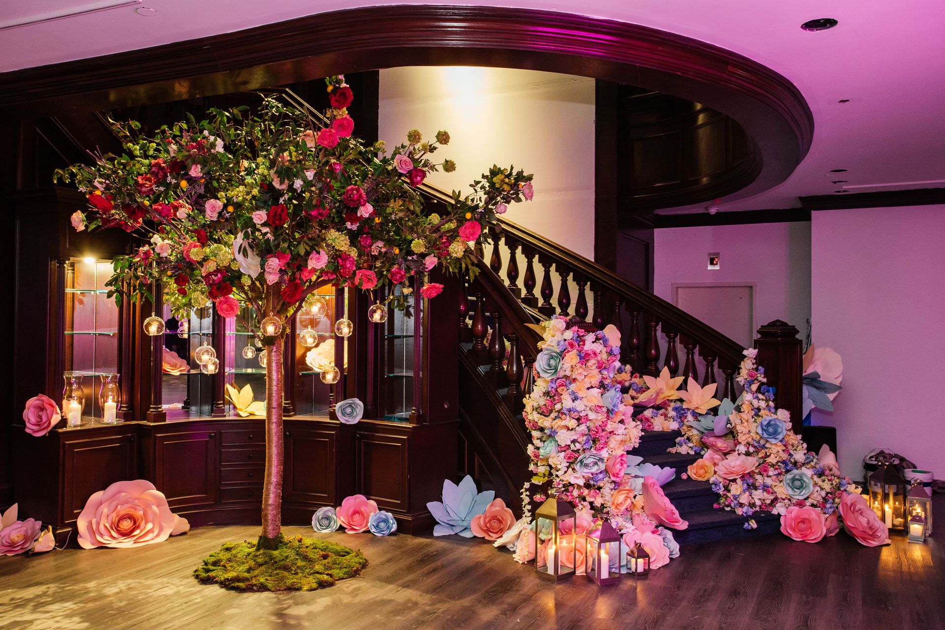 Staircase with decorative paper flowers next to a free standing tree with flowers and hanging ornaments