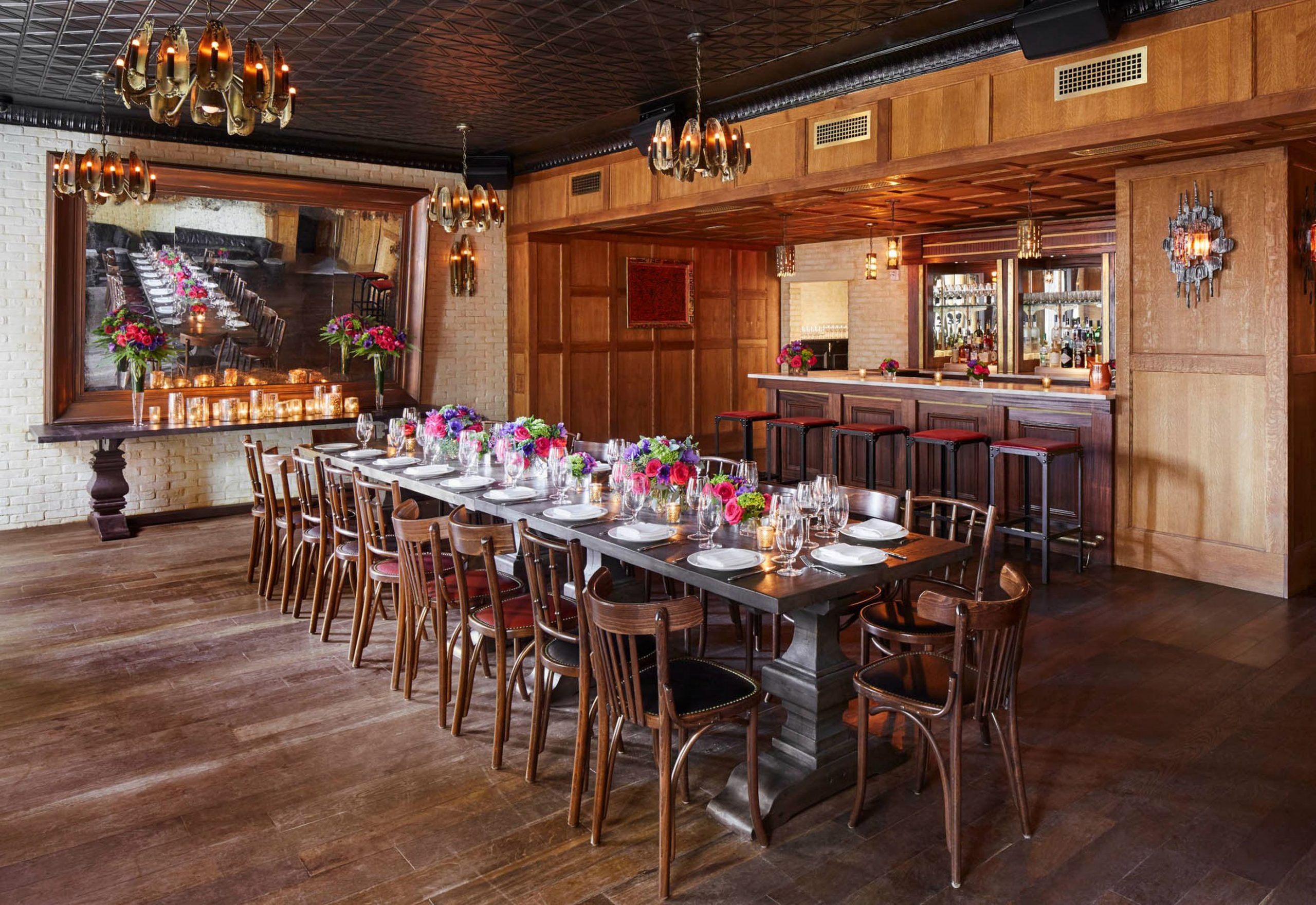 Long wooden table with colorful flower arrangements in front of a large wooden mirror