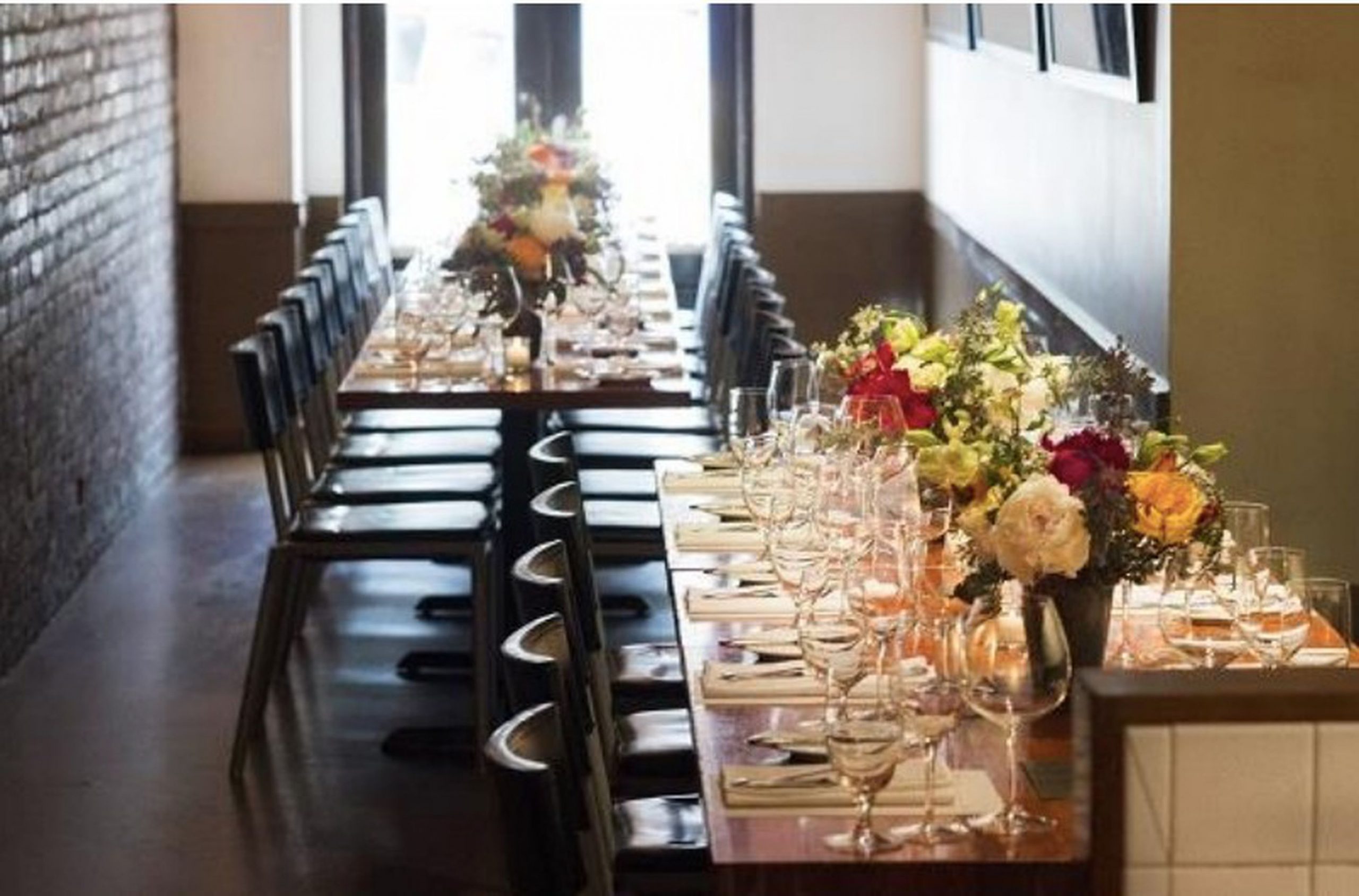 Two dining tables set with glasses, flatware and large floral arrangements