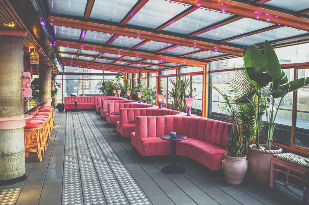 Enclosed rooftop venue with lush coral lounge couches and bar stools