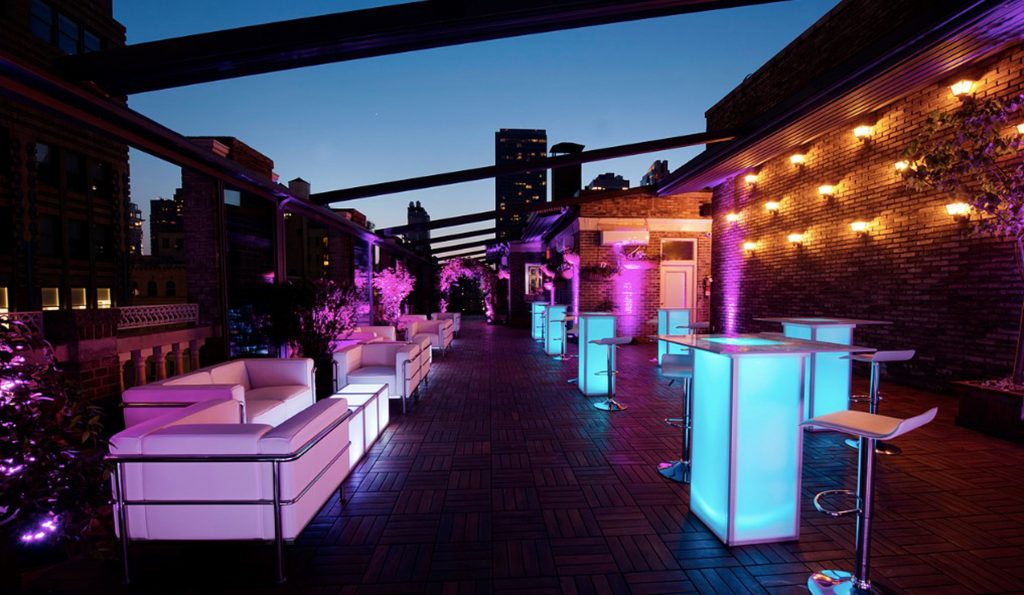 A rooftop venue at night with white lounge areas and light up high boys