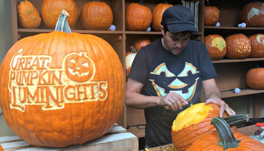 Man carving large pumpkins with one pumpkin that says "Great Pumpkin Luminights"