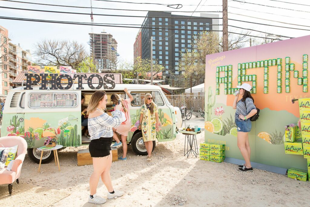 A retro sanded booth with a 1970s van and a photo moment wall that says "Austin" in green LaCroix cans