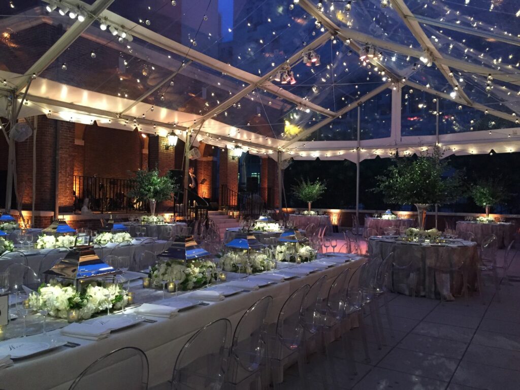 Long rectangular tables and circle tables with white linens under a see through tent