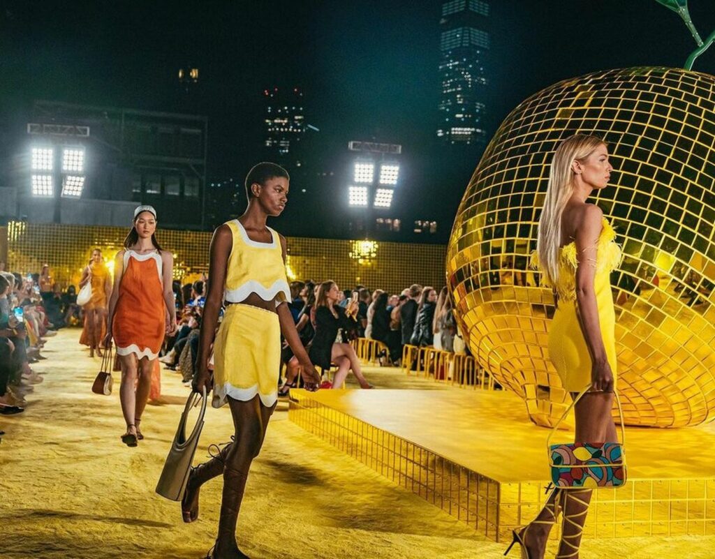 Models walking on a yellow runway at a nighttime fashion runway show