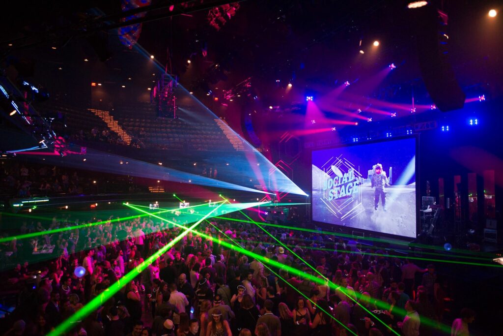 Large space with a huge crowd, a big screen that says "Social Stage" and neon lights