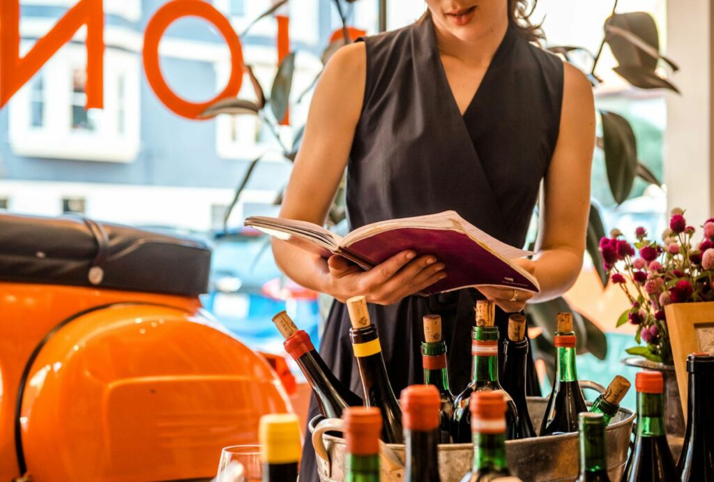 Woman standing over bottles of wine reading a book