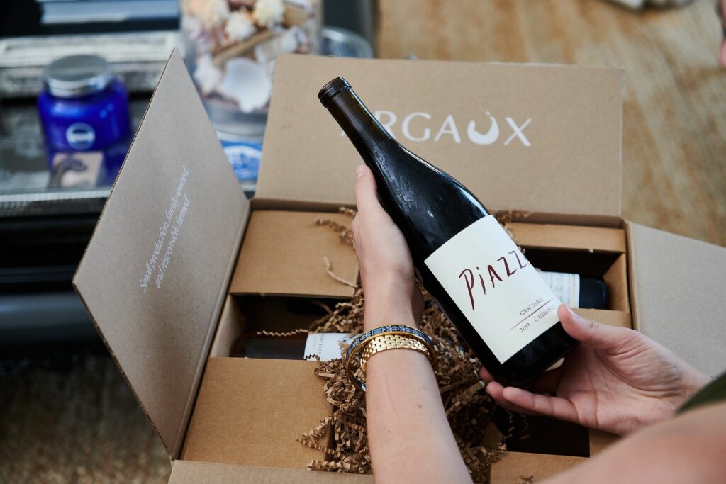 Hands holding a bottle of wine over an open box.