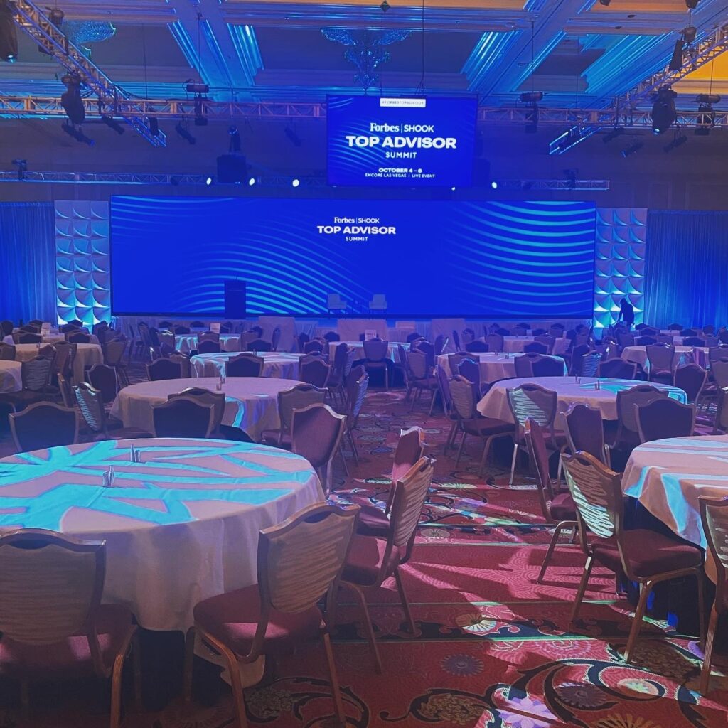 Large conference room with round tables set in front of a large video screen