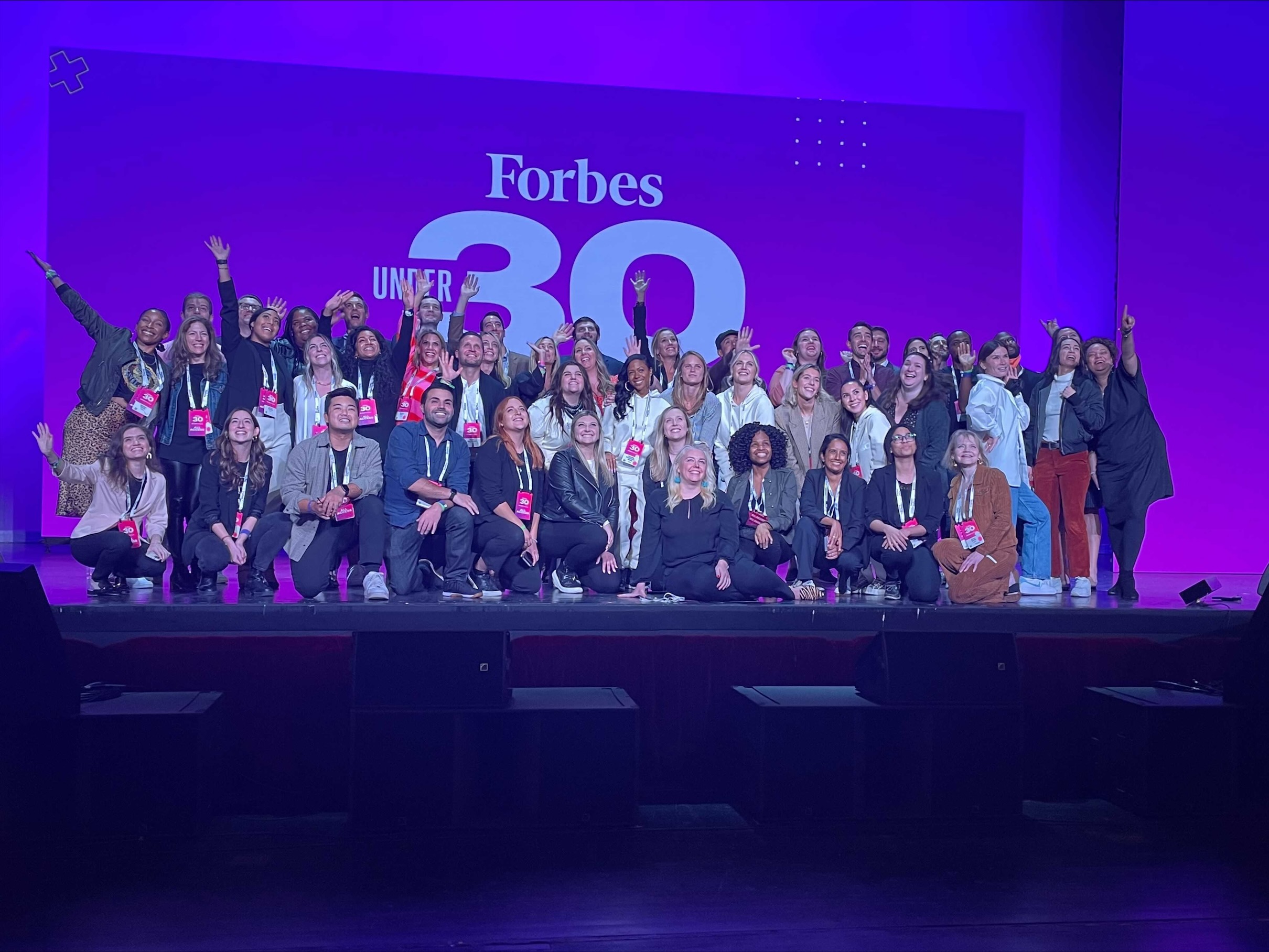 Group of people on stage in front of a sign that says Forbes 30