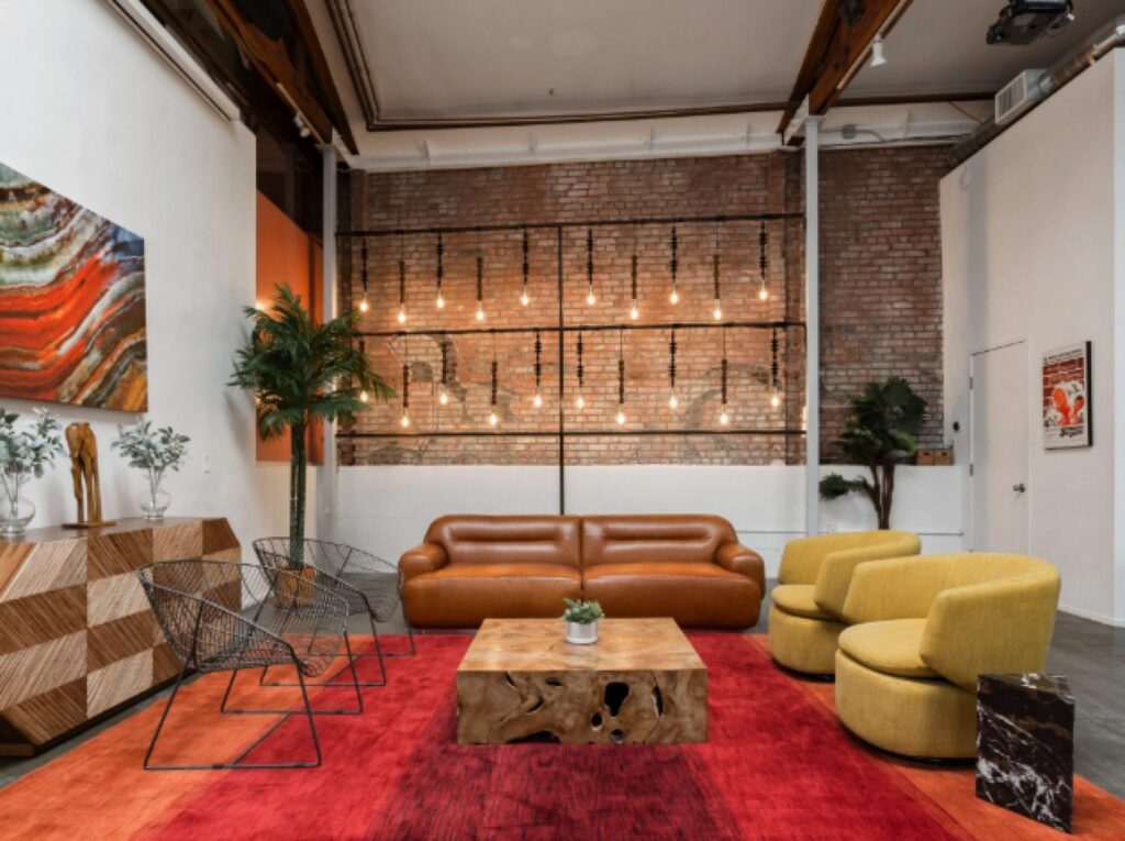 Room with red rug, yellow chairs, leather couch, and exposed brick wall