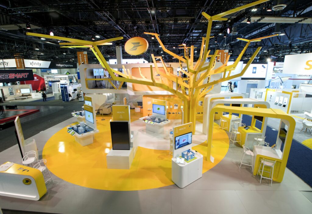 Large yellow and white booth at a conference with large yellow tree structure in the middle