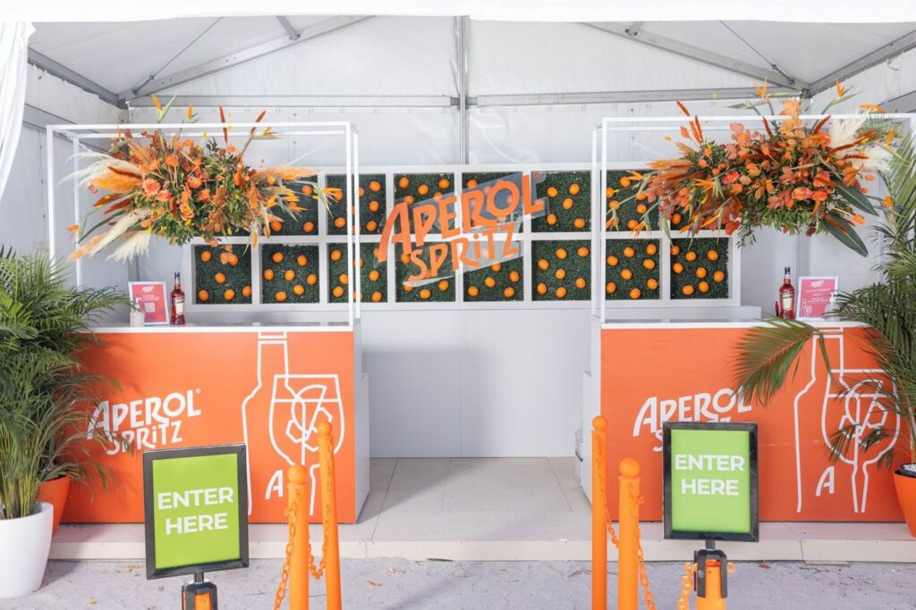 A colorful orange, green, and white booth with two bars that say "Aperol Spritz" 