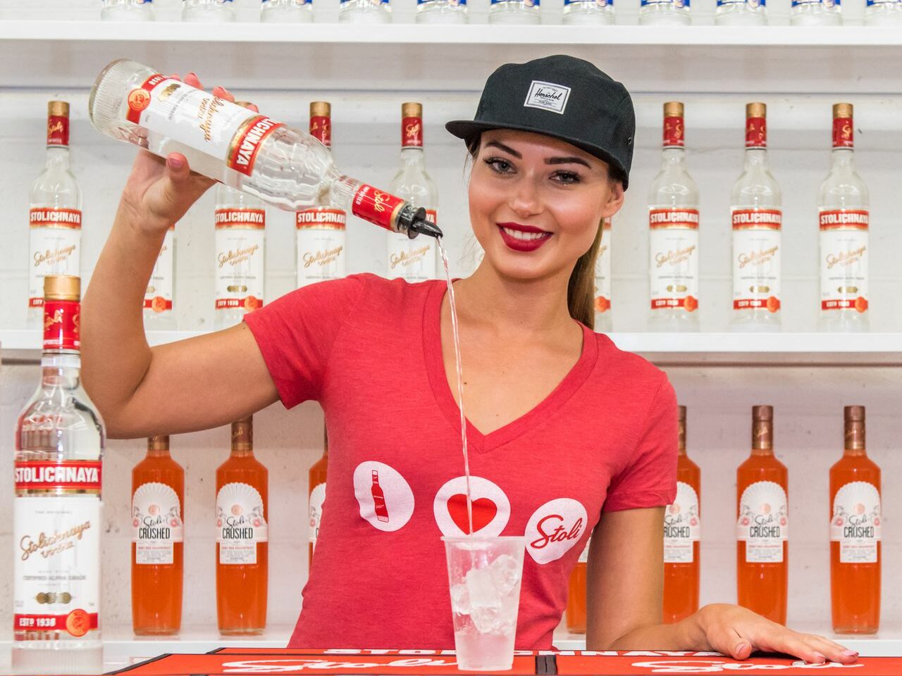 A woman pouring a drink at a bar lined with Stoli bottles 