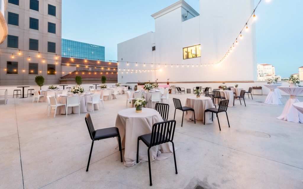 Sprawling rooftop restaurant with small tables and black and white chairs under string lights