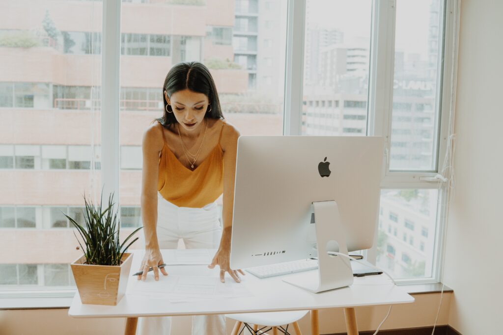 A brunette woman standing over a desk and computer