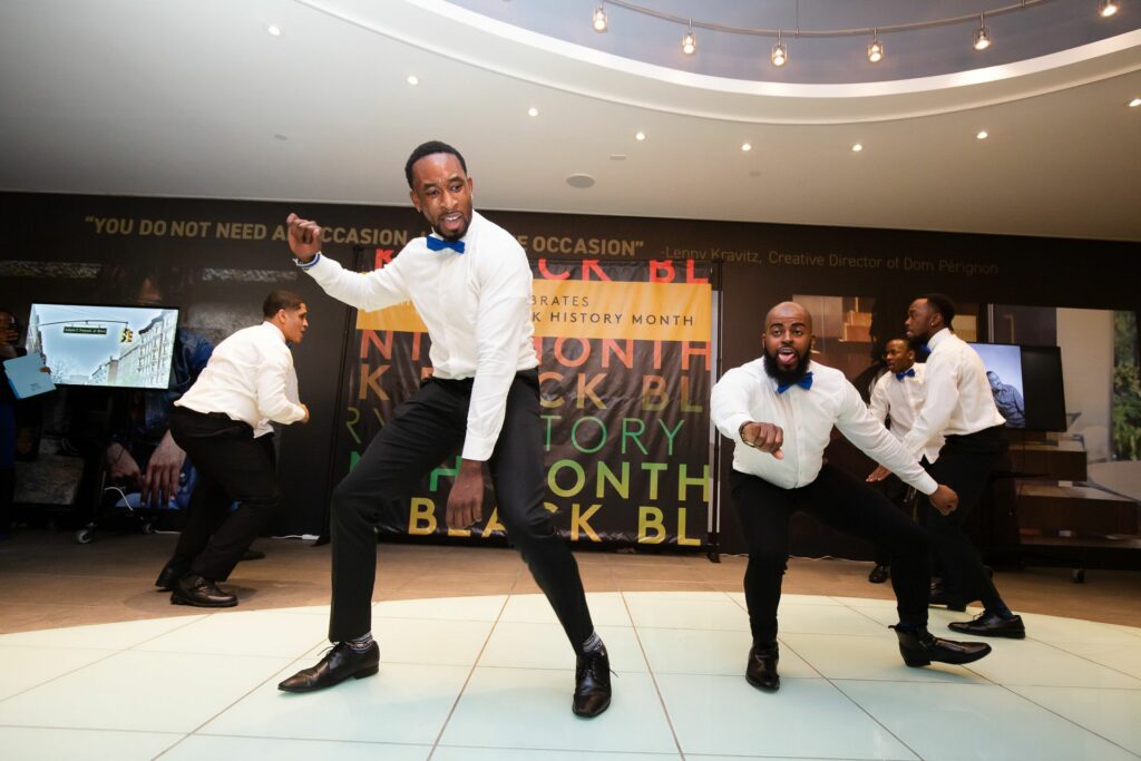 Two black men dancing in black dress pants and white button ups at a Black History Month Event