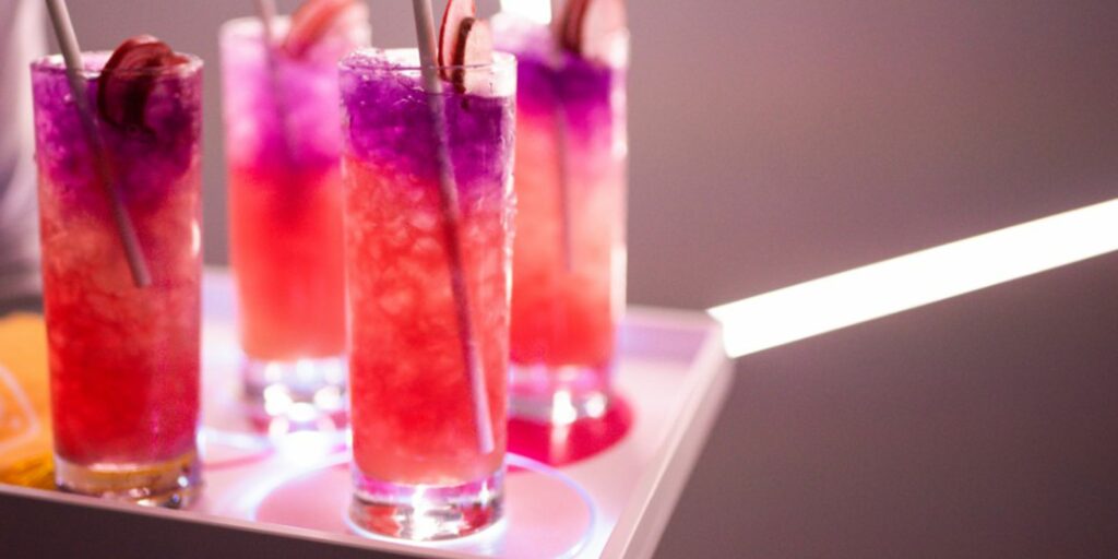 A tray of colorful red and purple cocktails with straws