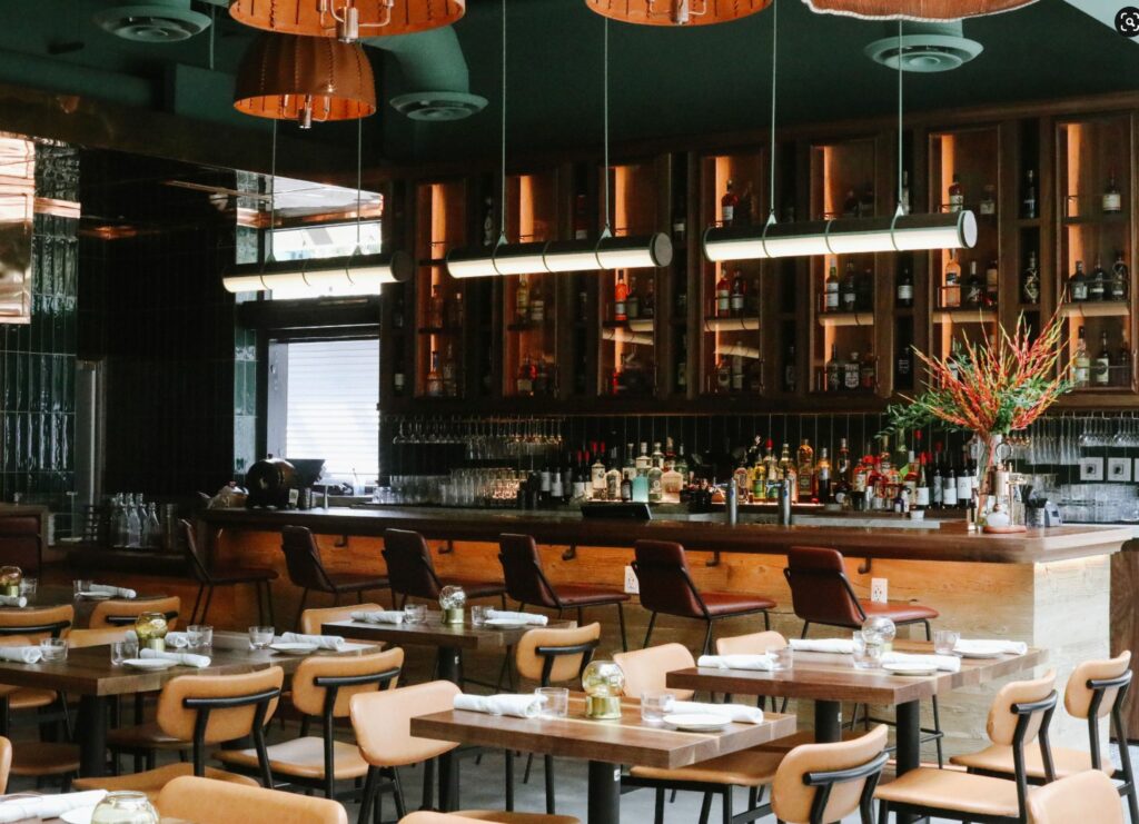 A restaurant dining room with wooden tables and chairs and a large, tall bar area