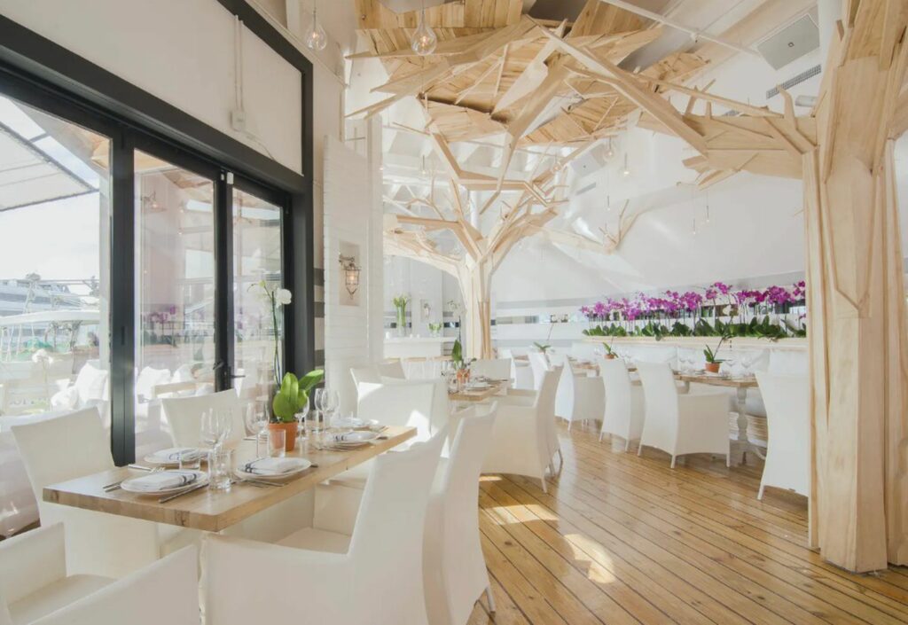 A very light and open dining space with white chairs and many orchids