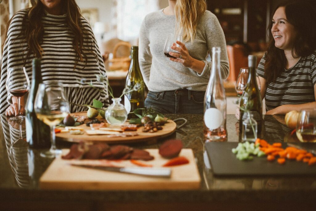 Three woman around a table of food and wine