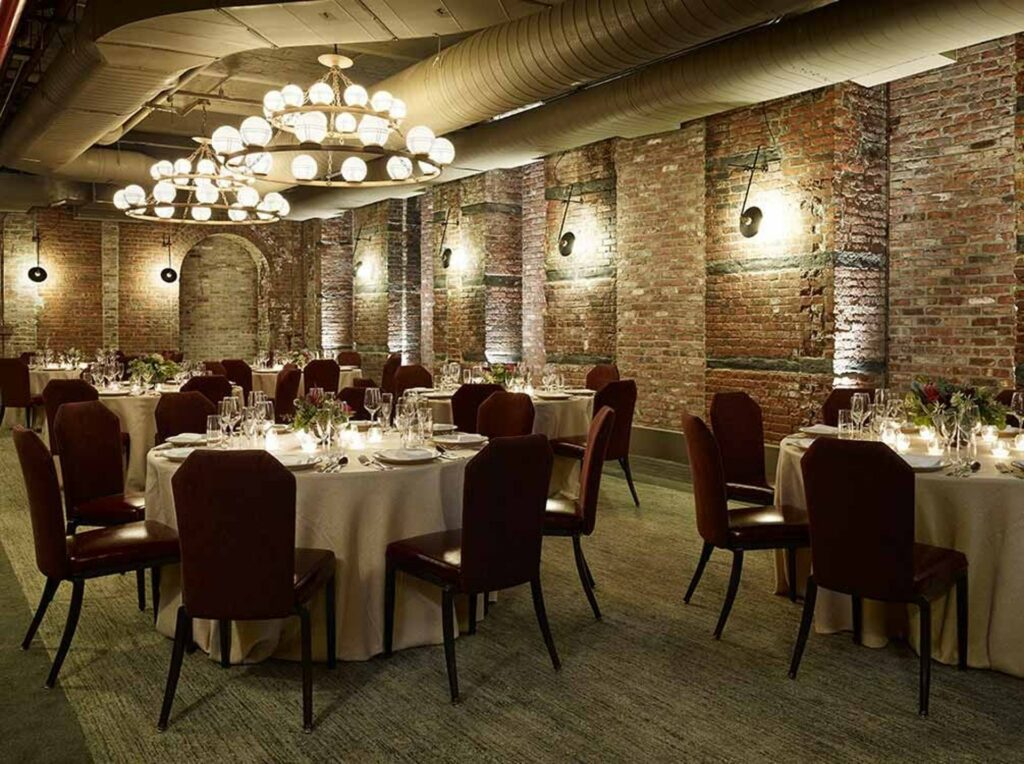 One of The Beekman's private dining rooms in NYC with white table cloths, brick walls, and dim lighting. 