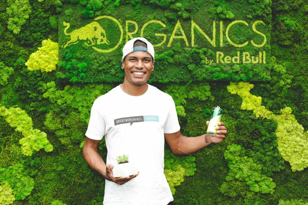 Man posing with a an and plant in front of a greenery wall 