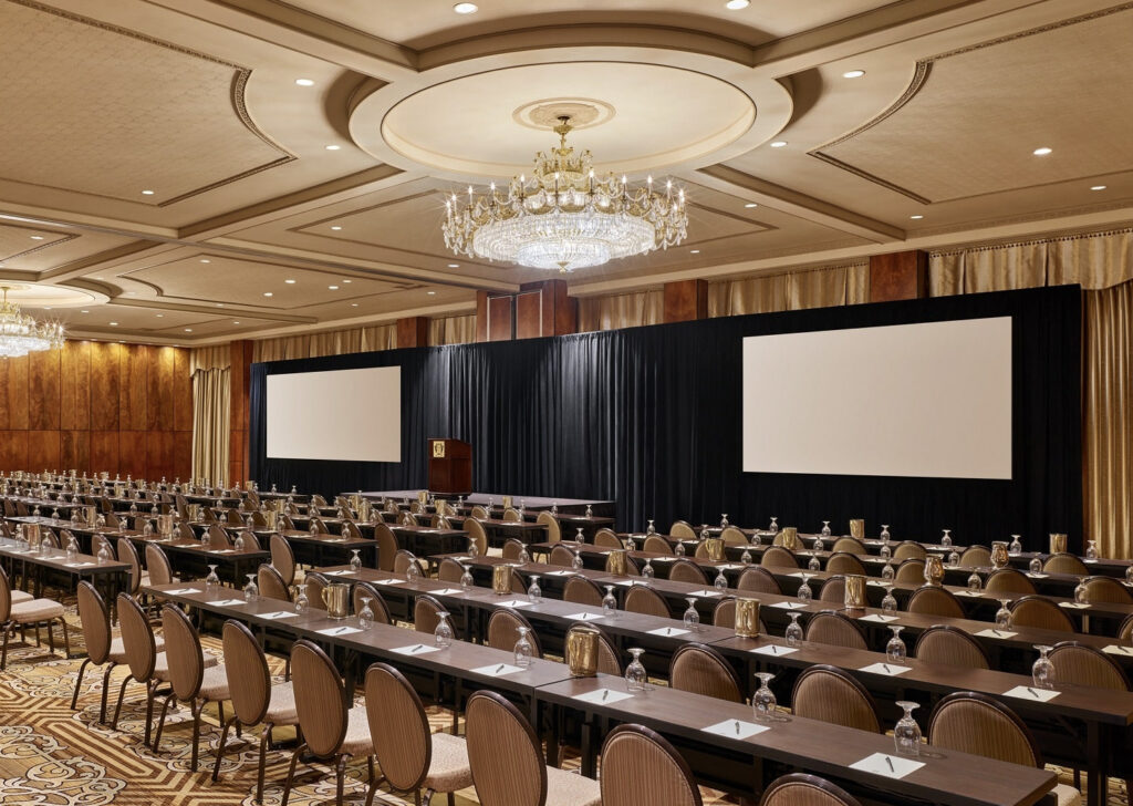 Conference and ballroom with chairs and tables lined up with large chandelier and projectors