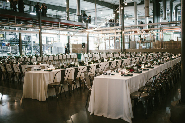 Large industrial venue with long tables with white table cloth and string lights