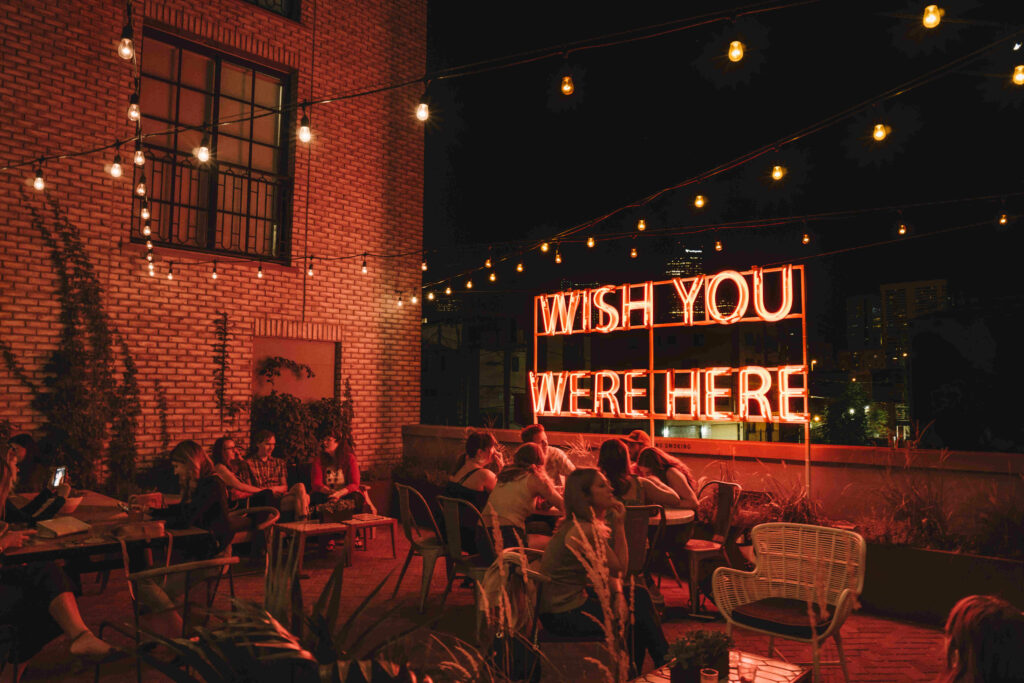 The Ramble Hotel outside patio area at night with red lighting and Wish you were here neon sign