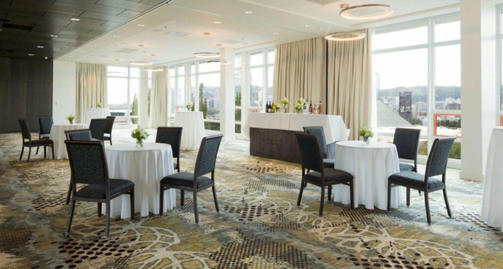 Hotel ballroom with dining tables with white table cloth and floral centerpiece overlooking city 