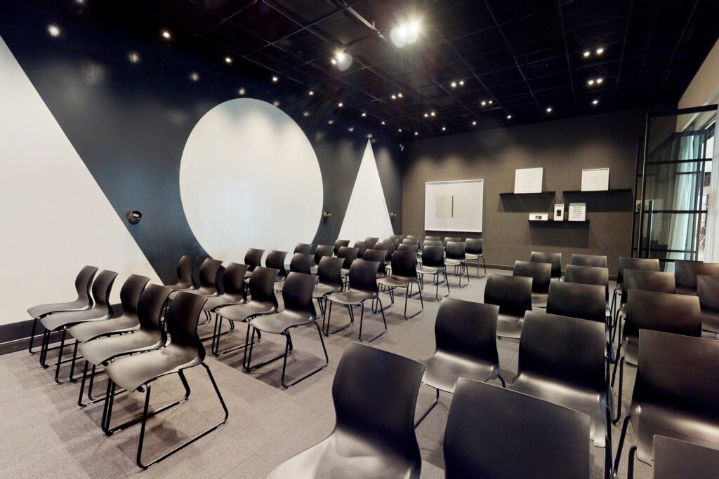 Black chairs in rows in a meeting space with black and white geometric shapes on the wall