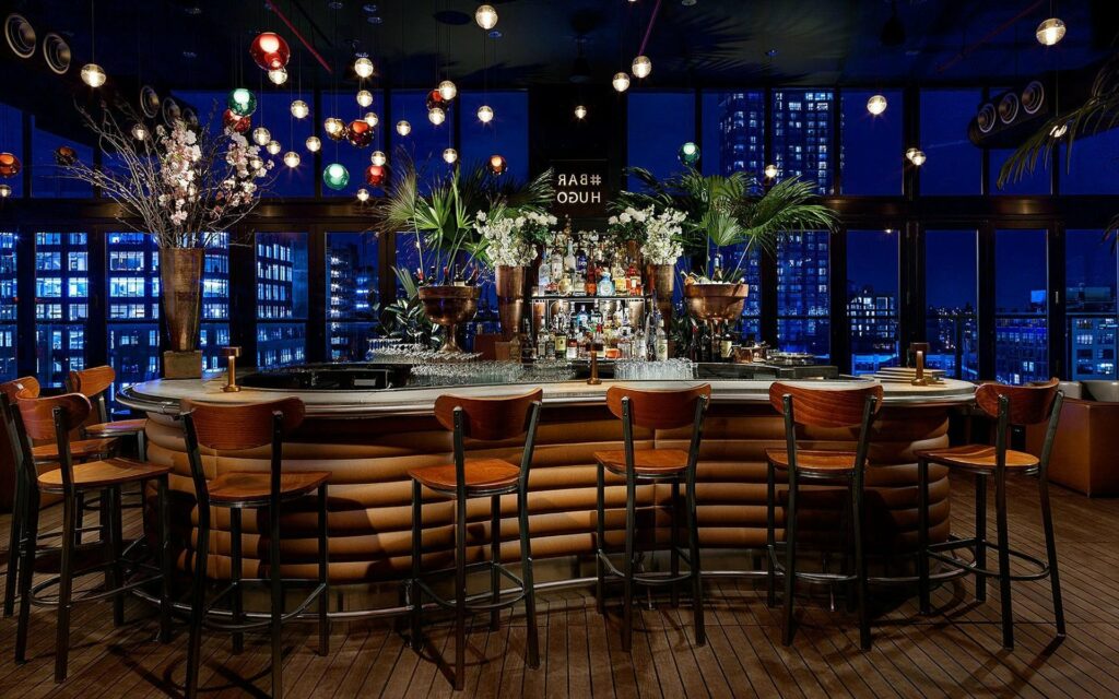 The bar area of Hotel Hugo at night with a view of the city skyline