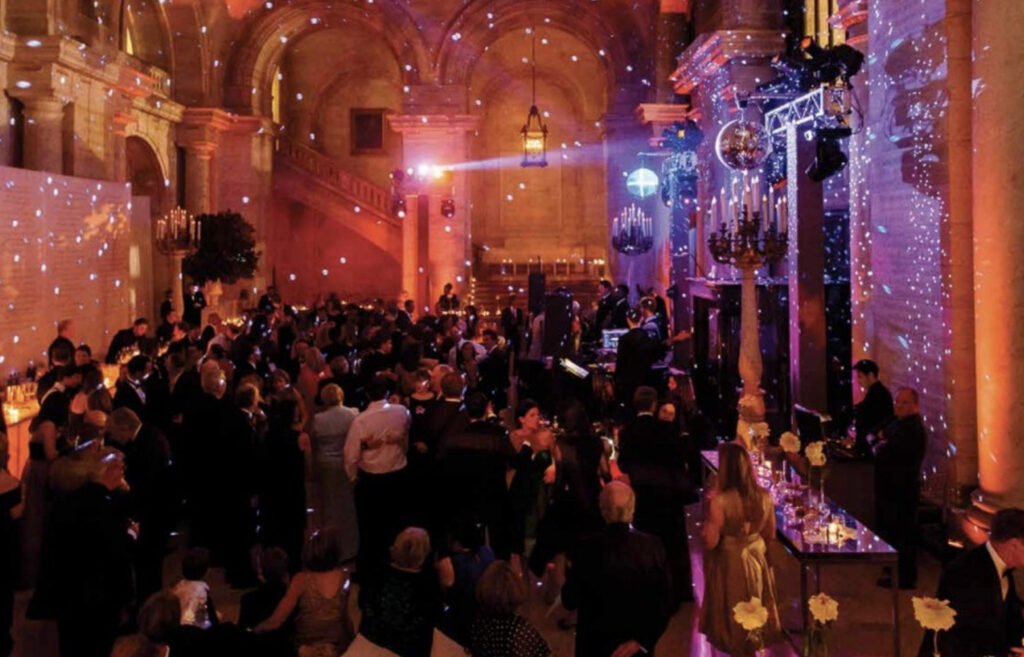 Vaulted room filled with people with disco balls and party lighting 