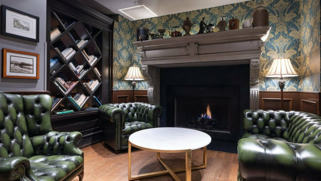 The Long Room bar in NYC with green leather chairs and a roaring fireplace