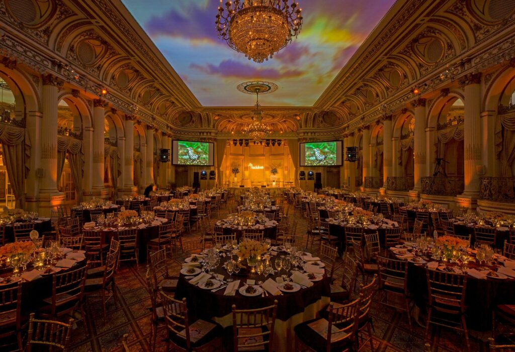 Huge ornate event hall with banquet tables and chandelier with projected sunset ceiling