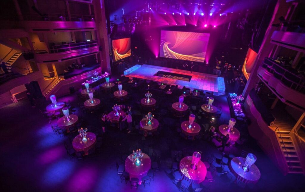 round tables on dance floor in front of a stage with blue and pink lighting 