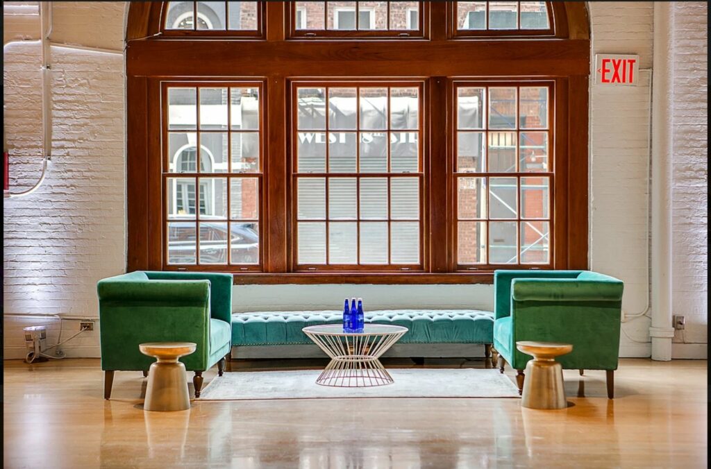 Large window above green lounge furniture with white brick walls and wood floors