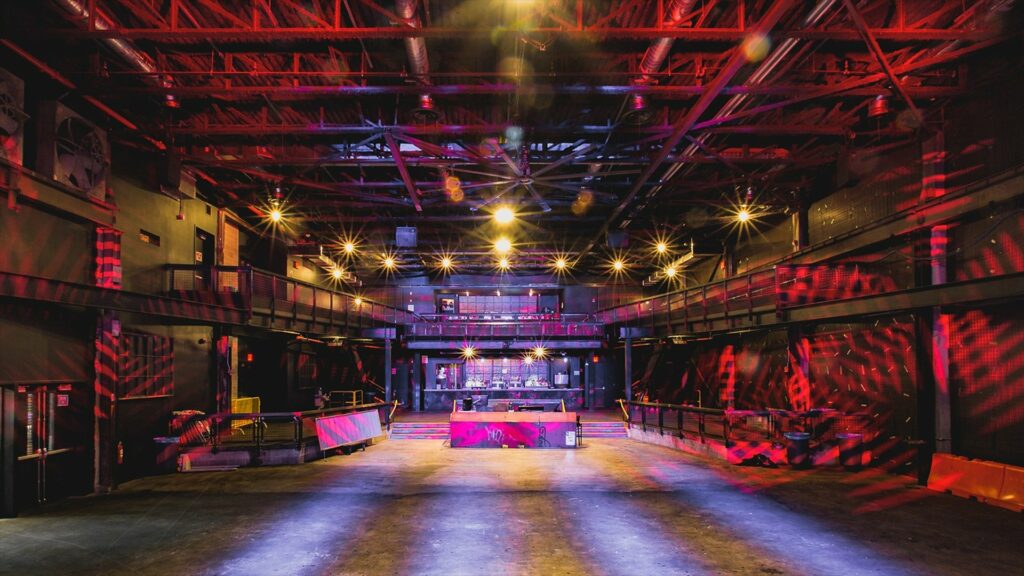 Raw concert space with red textured projections on the walls and overhead trussing