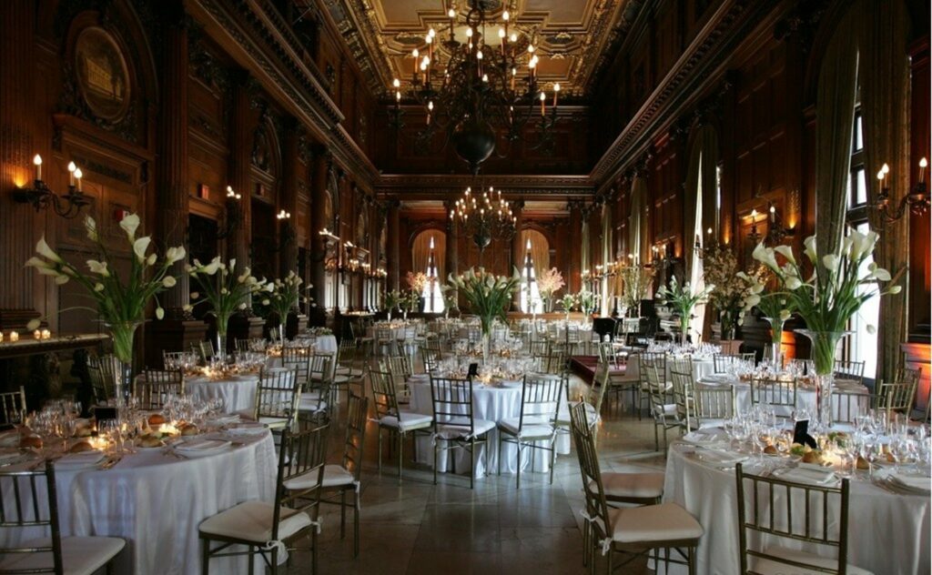 Elegant room with chandelier and banquet tables with gold chairs and white tablecloths and white floral centerpieces