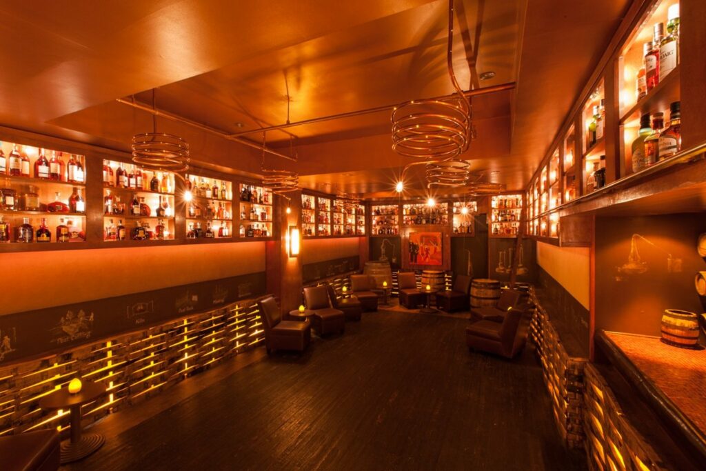 Private room with wood floors and leather lounge seating surrounded by illuminated shelves of brandy bottles
