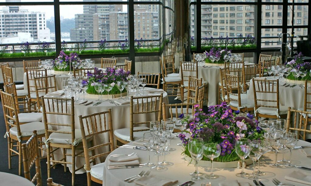 Round banquet tables with purple flowers and gold chairs with windows overlooking the city