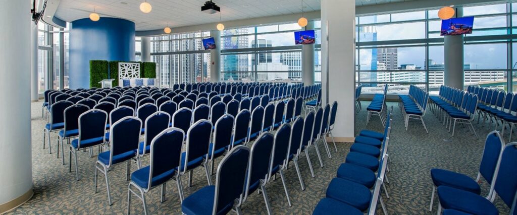 Amway Center event space with rows of blue chairs and windows with a stage and podium