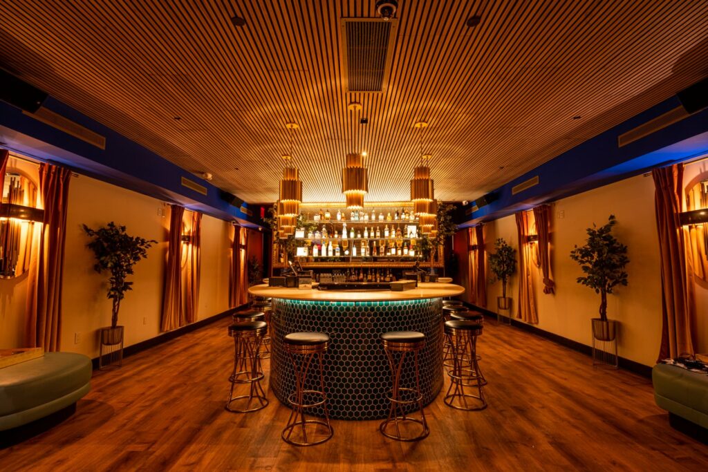 Glamorous circular green tiled bar with wood slat ceiling and amber lighting