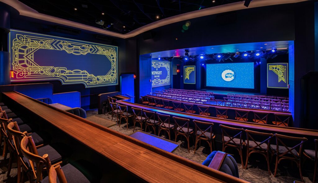 large stage and rows of seating with blue projection screen and walls illuminated
