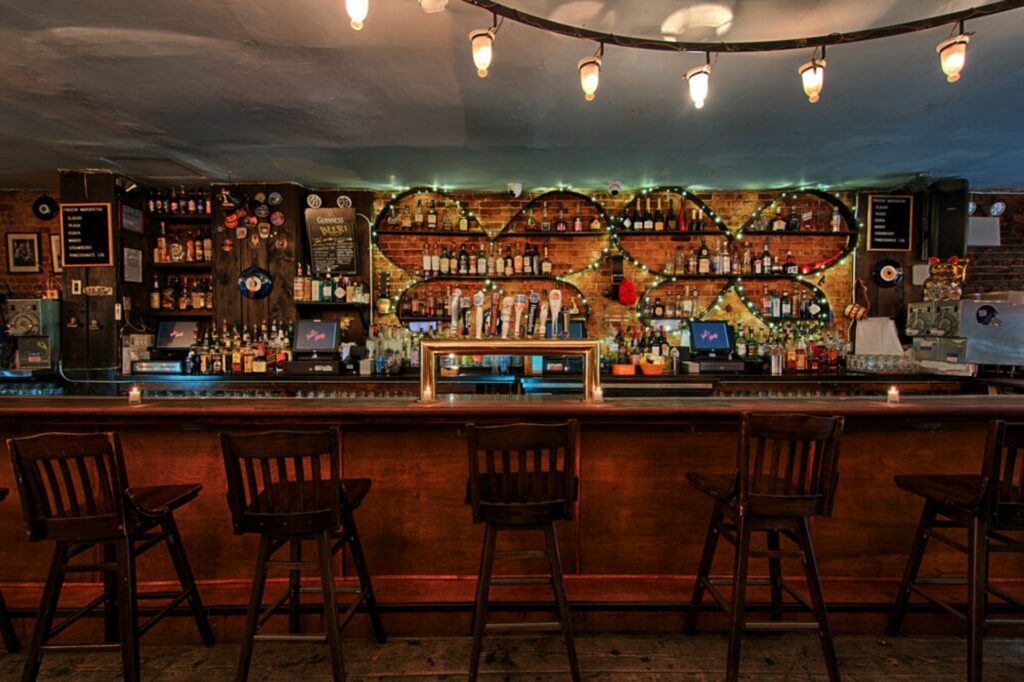 Campy bar with wooden floors and barstools and string lights round bottles