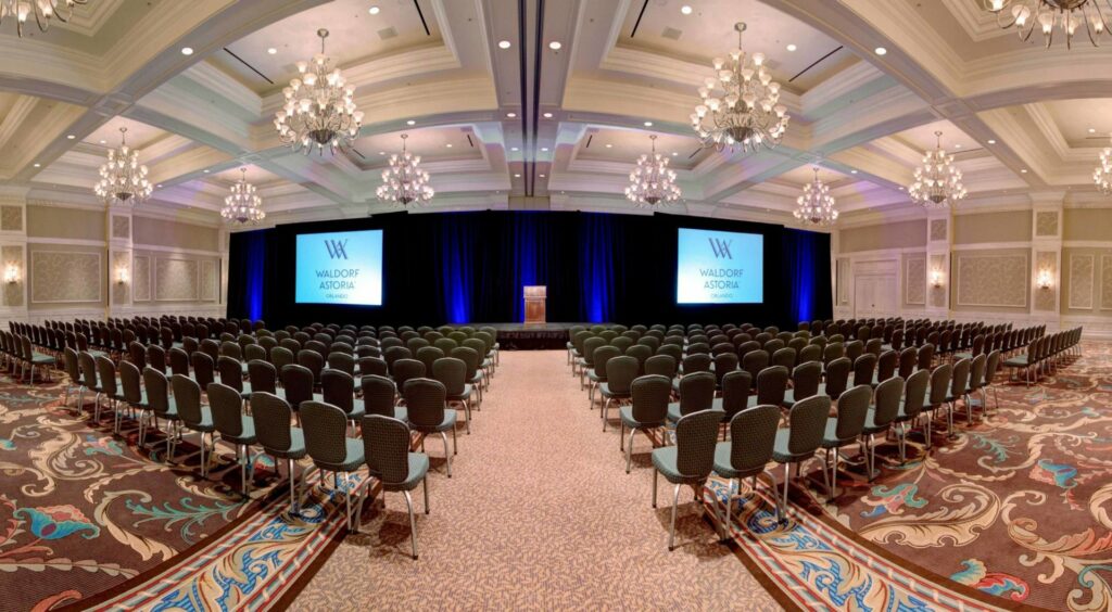 Waldorf Astoria Orlando ballroom event space set up for a conference with rows of chairs and a blue stage with two projected screens and podium